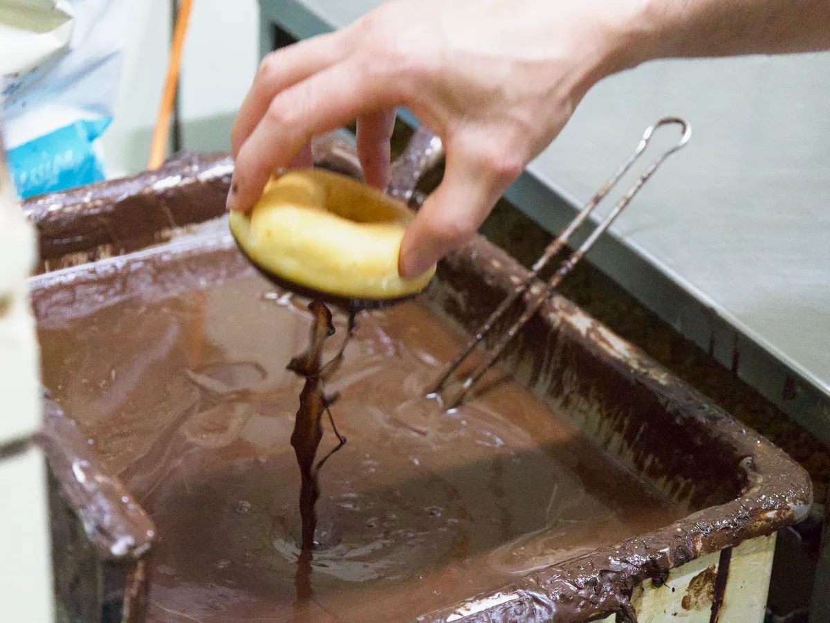 Ein Donut wird in der Backstube in Schokoladenglasur getaucht
